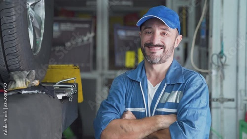 Worker in uniform holds wrench, car service. Mechanic looking up at camera at the repair garage.