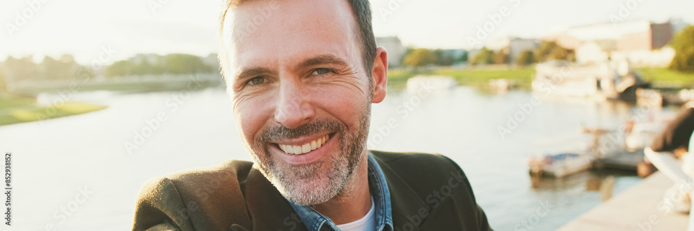 Fototapeta premium Close up, man makes selfie on mobile phone on the embankment of the river. Backlight