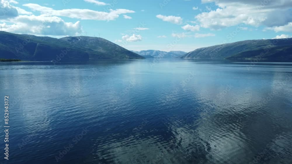 flying over calm blue fjord with mighty mountain in the background with windmill farm on top and pleasure boat moving over the water, aerial video flying over calm blue fjord with mighty mountain in the background with windmill farm on top and pleasure boat moving over the water, aerial video