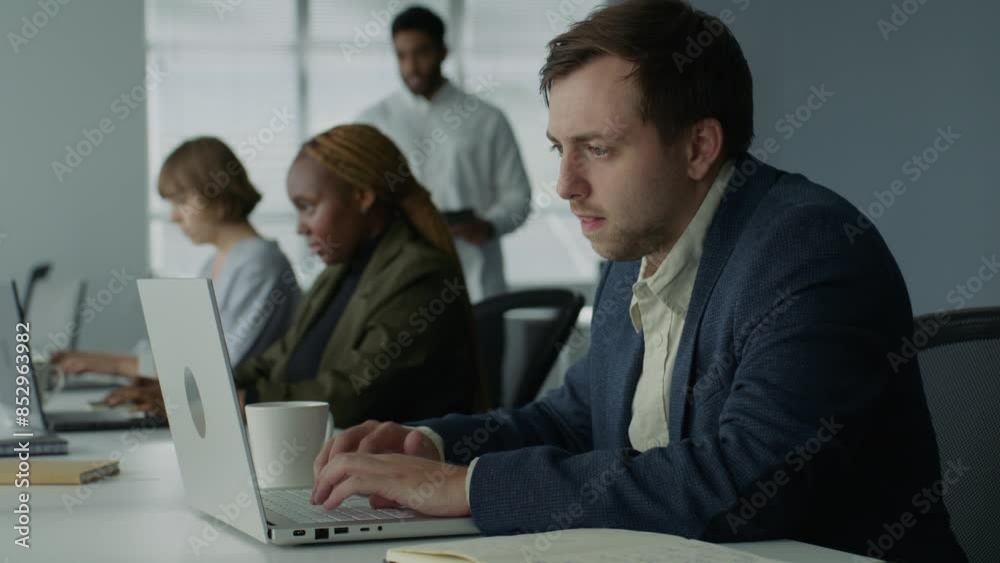 Four young adults in businesswear working on laptops and drinking coffee at desk in office Four young adults in businesswear working on laptops and drinking coffee at desk in office