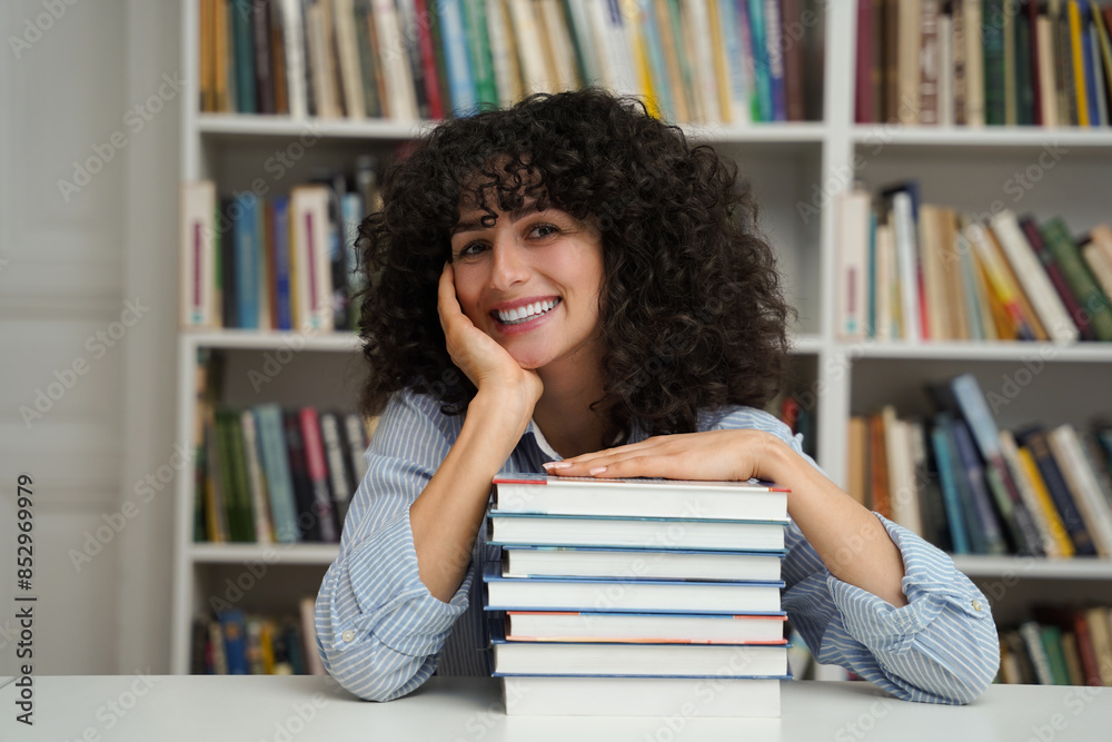 Cheerful student girl sitting at desk with stack of books in library Cheerful student girl sitting at desk with stack of books in library