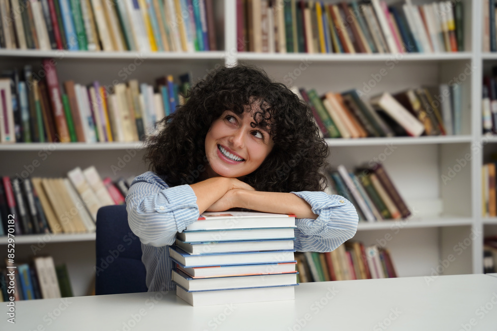 Cheerful student girl sitting at desk with stack of books in library Cheerful student girl sitting at desk with stack of books in library