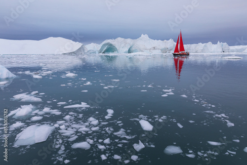 Red sailing boat in front of a giant white Iceberg with an arch, in Ilulissat Icefjord in Greenland photo