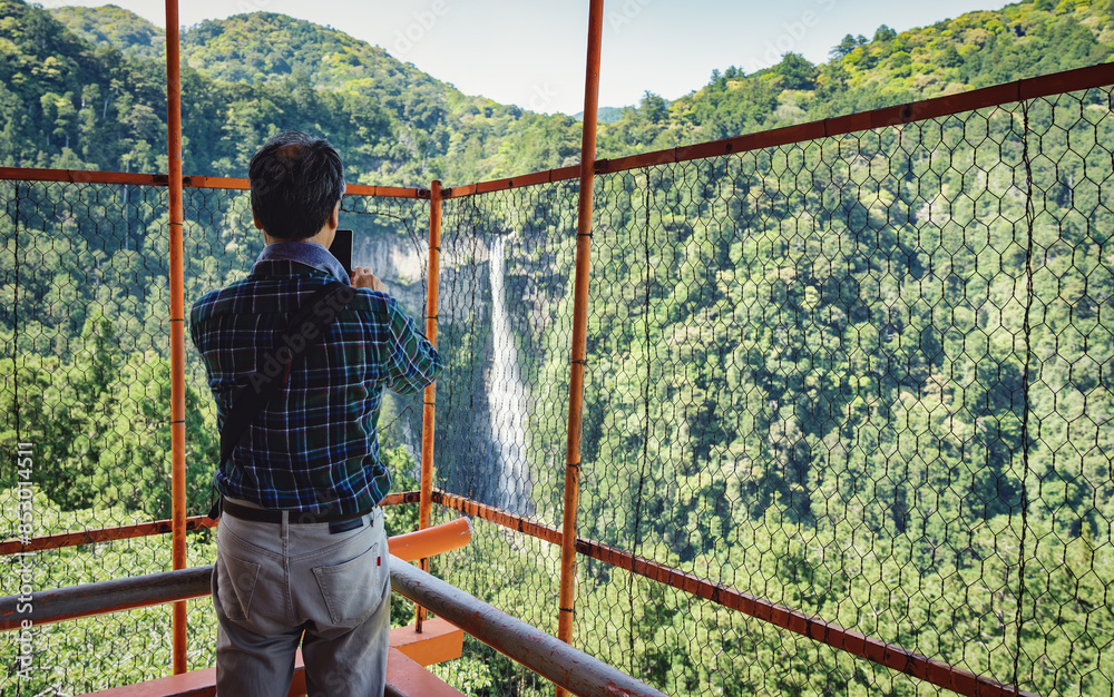 Back view with a tourist taking a picture with Nachi Waterfall located in Nachikatsuura, Wakayama, Japan Back view with a tourist taking a picture with Nachi Waterfall located in Nachikatsuura, Wakayama, Japan