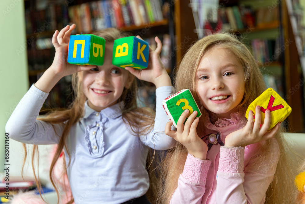 Two funny girls have fun playing with alphabet cubes Two funny girls have fun playing with alphabet cubes