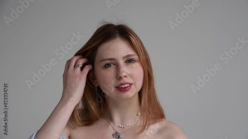 Close-up portrait of beautiful smiling caucasian redhead woman with naked shoulders against grey background. Real time handheld video. Beauty and skincare theme.
