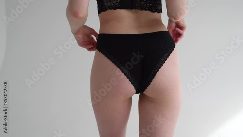 Close-up view of sexy slim caucasian woman standing against grey background. Woman wears black lace panties. Soft focus. Real time video. Fashion and sensuality theme.
