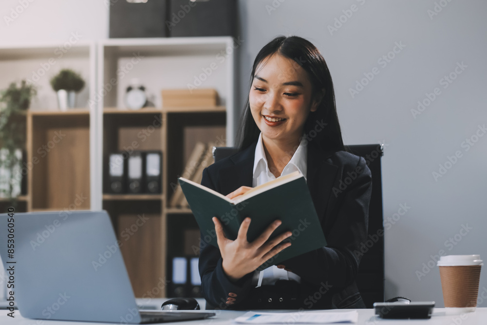 Happy young Asian businesswoman working on laptop and taking notes In office. Happy young Asian businesswoman working on laptop and taking notes In office.
