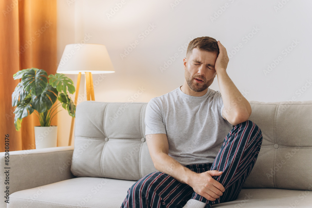 Young man suffering from headache at home, touching his temples, copy space, blurred background. Migraine, headache, stress, tension problem, hangover concept Young man suffering from headache at home, touching his temples, copy space, blurred background. Migraine, headache, stress, tension problem, hangover concept