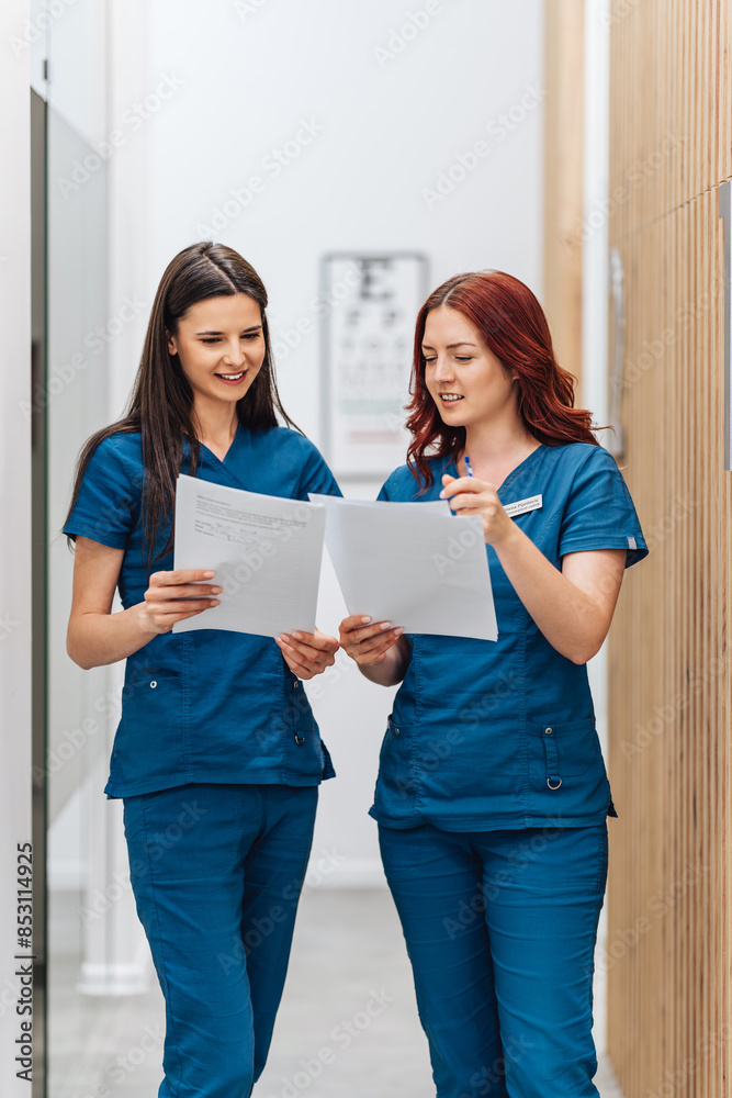 Two beautiful and serious female doctors or a technicians standing in a modern clinic for diagnosis and treatment of eye diseases and reading documents. Healthcare and medical concept. Two beautiful and serious female doctors or a technicians standing in a modern clinic for diagnosis and treatment of eye diseases and reading documents. Healthcare and medical concept.
