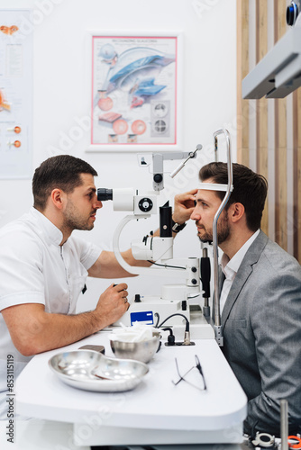 Attractive male doctor ophthalmologist is checking the eye vision of handsome middle age man in modern clinic. Doctor and patient during medical check up in ophthalmology clinic.