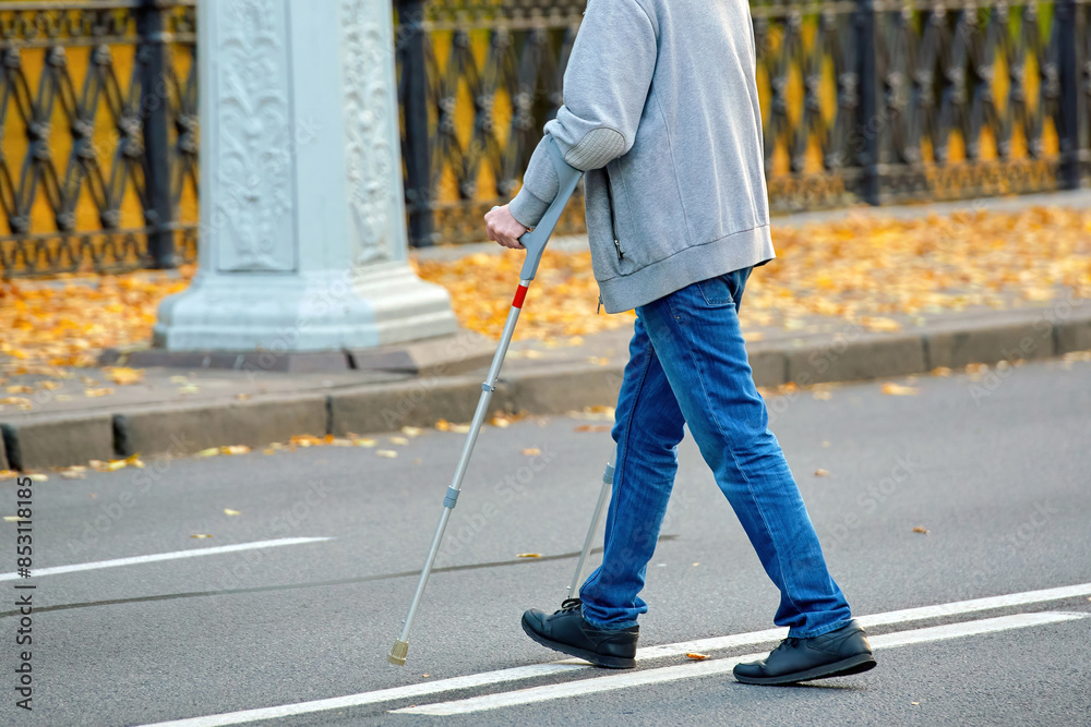 Man crossing the road on crutches, violation of pedestrian safety rules in an urban environment. Man with crutches navigating road crossing, violation of pedestrian safety regulations..