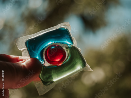 Laundry detergent pod. Men hand holds colorful water soluble sachet. Packs or liquitabs are water-soluble pouches containing highly concentrated laundry detergent, softener and other laundry products photo