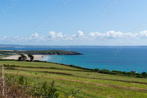 La plage de la presqu'île de Crozon s'étend vers la pointe du Bellec sous un ciel bleu ponctué de quelques nuages blancs, avec la mer d'Iroise en arrière-plan.