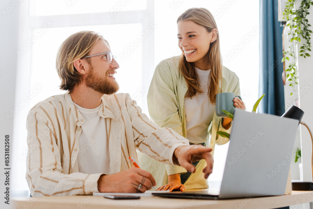 Young happy couple using laptop and smiling while working from home office Young happy couple using laptop and smiling while working from home office