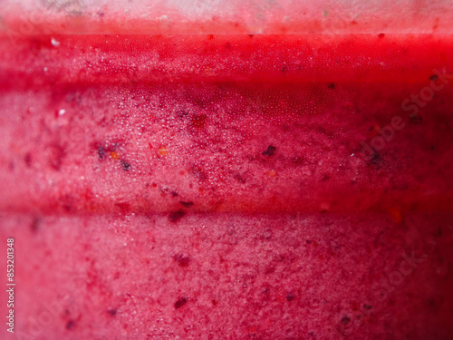 A macro shot of a pink red berries smoothie in a cup, showcasing its detailed texture and vibrant color.
