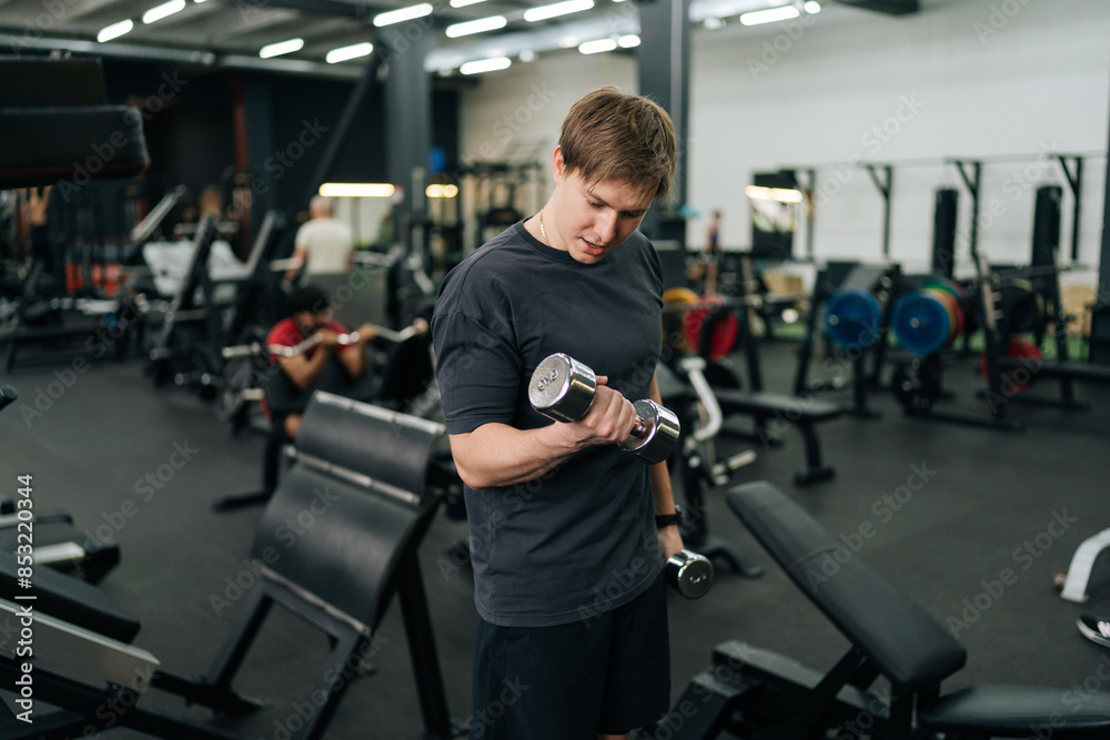 Motivated beginner sportsman doing exercises with weight at gym. Athletic male performing functional training with dumbbells to tone his muscles. Concept of healthy lifestyle, physical sport activity. Motivated beginner sportsman doing exercises with weight at gym. Athletic male performing functional training with dumbbells to tone his muscles. Concept of healthy lifestyle, physical sport activity.