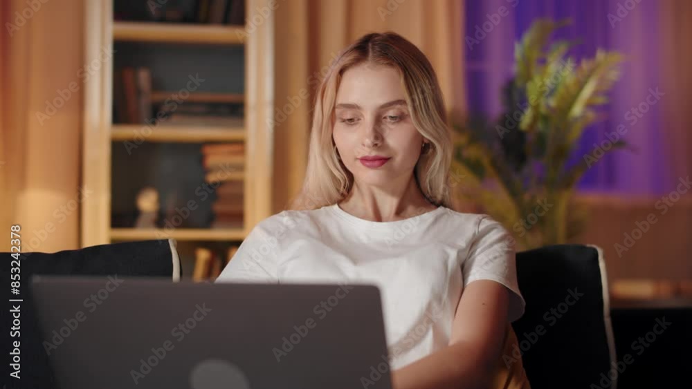 A young woman is sitting at her cozy home, working on her laptop during the night A young woman is sitting at her cozy home, working on her laptop during the night