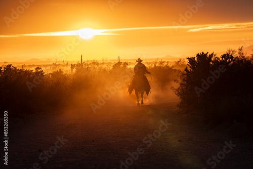 Silhouette of ranch hand, or cowboy, riding his horse in the sunset.