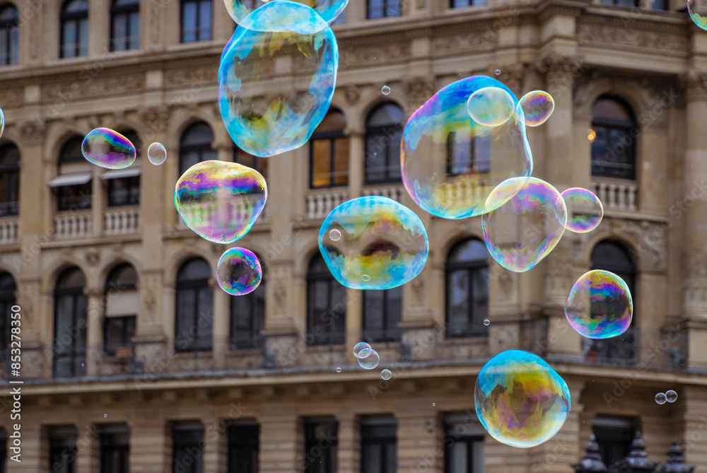 Many multicolored giant soap bubbles flying in the air on a windy day. Huge bubble are stretching on the wind into long smoothy changing form without popping. Close up. Copy space. Selective focus.