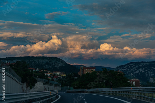 inquadratura di parte dell'ambiente misto urbano e naturale tra la collina e la città, vicino a Trieste, nel nord est Italia, con un cielo azzurro ricco di nuvole colorate di arancione al tramonto