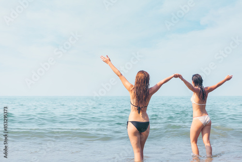 Two Women Enjoying the Ocean Waves.Two women in bikinis, joyfully playing in the ocean waves. summer day at the beach. © Svetlana Radayeva