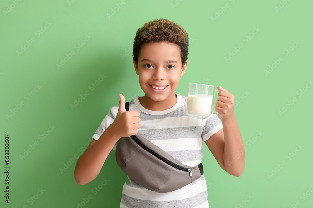Little African-American boy with glass cup of milk showing thumb-up on green background Little African-American boy with glass cup of milk showing thumb-up on green background