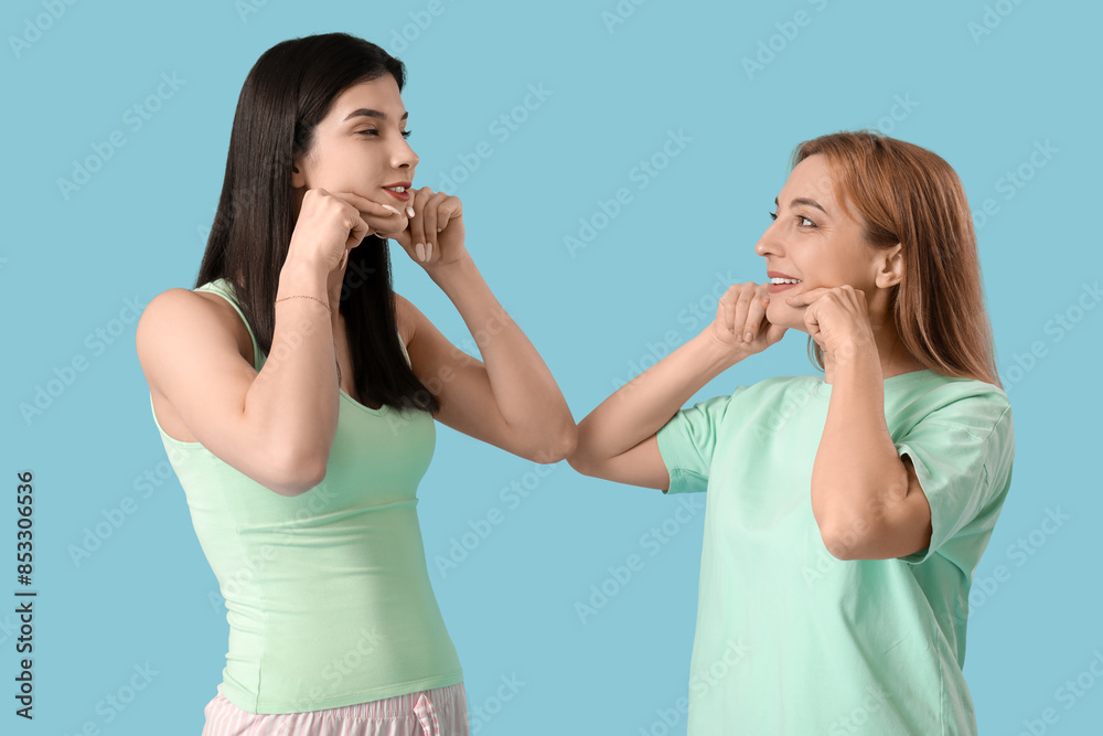 Beautiful happy women doing face building exercise together on blue background Beautiful happy women doing face building exercise together on blue background