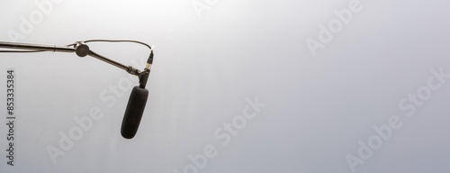 Simple black studio mic, microphone hanging placed on a long high top mic arm stand, plain gray simple background wide copy space, audio voice recording studio, live symbol, abstract concept, nobody