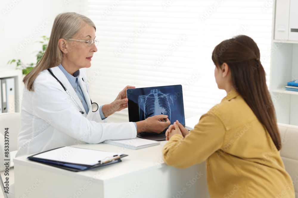 Lung cancer. Doctor showing chest x-ray on laptop to her patient in clinic Lung cancer. Doctor showing chest x-ray on laptop to her patient in clinic