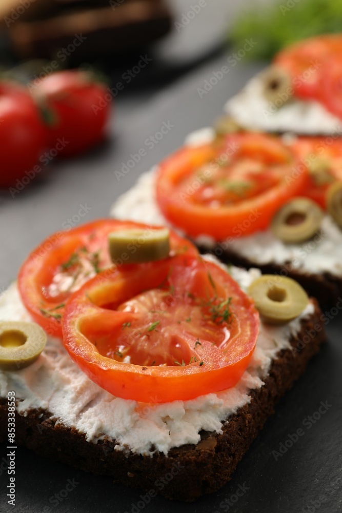 Delicious ricotta bruschettas with sliced tomatoes, olives and greens on black table, closeup