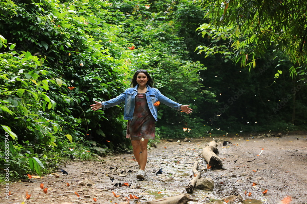 Naklejka premium A young lady wearing a short skirt with a butterfly print walks on the dirt road.There are swarms of butterflies along the way. Baan Krang Camp,KaengKrachan national park ,Phetchaburi,Thailand