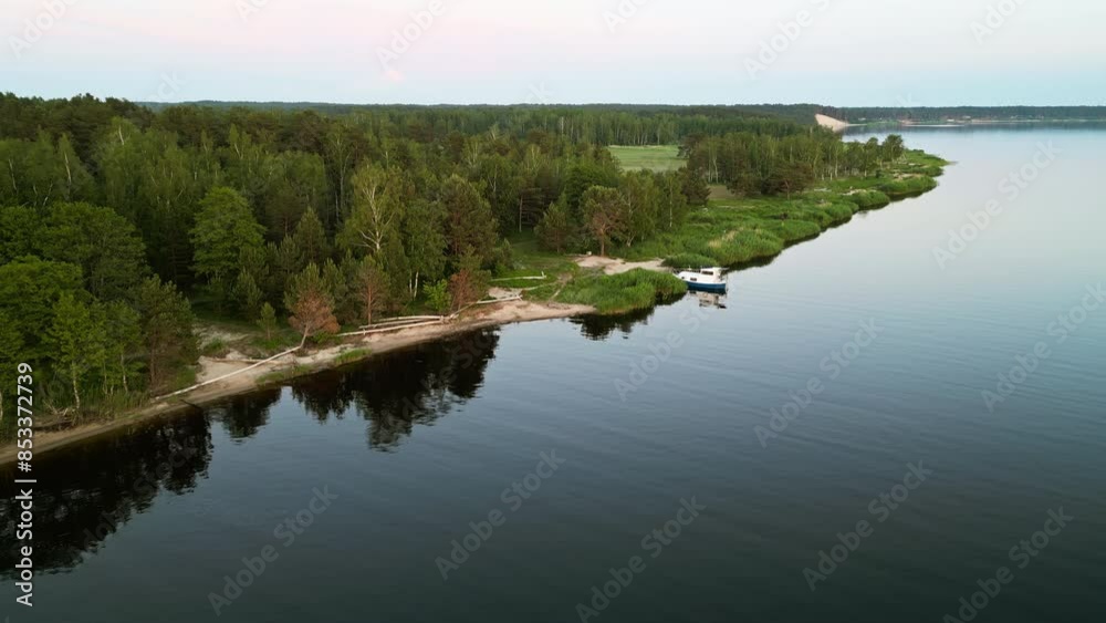 Aerial view captures serene beauty of forested lakeshore at sunset, offering a glimpse of peaceful nature