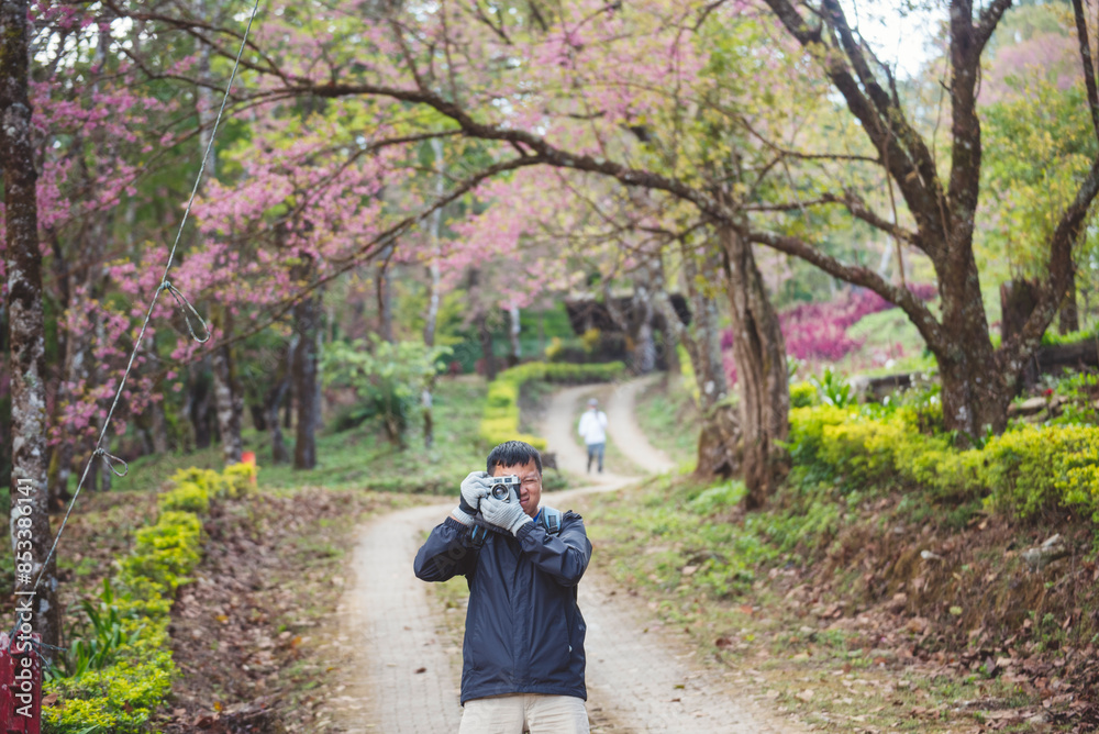 Asian man use professional digital camera take a photo. Smiling male photographer look at photo film camera outdoors. Mature adult man shooting photo in green nature park. Beautiful nature men hobby