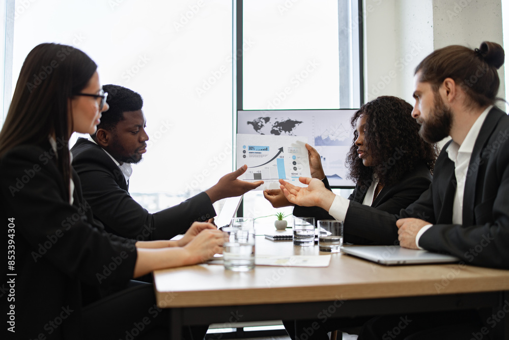 Business team consisting of four members discussing financial report during meeting. Professional setting with diverse team engaged in conversation. Focus on collaboration, teamwork, and analysis. Business team consisting of four members discussing financial report during meeting. Professional setting with diverse team engaged in conversation. Focus on collaboration, teamwork, and analysis.