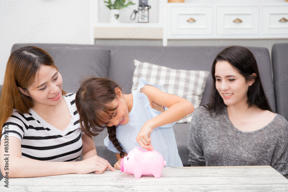 Mother teaching daughter saving with puts coins in piggy bank sitting on sofa in living room at home, mom and child learning about finance for wealth for future, household and money, family concept. Mother teaching daughter saving with puts coins in piggy bank sitting on sofa in living room at home, mom and child learning about finance for wealth for future, household and money, family concept.