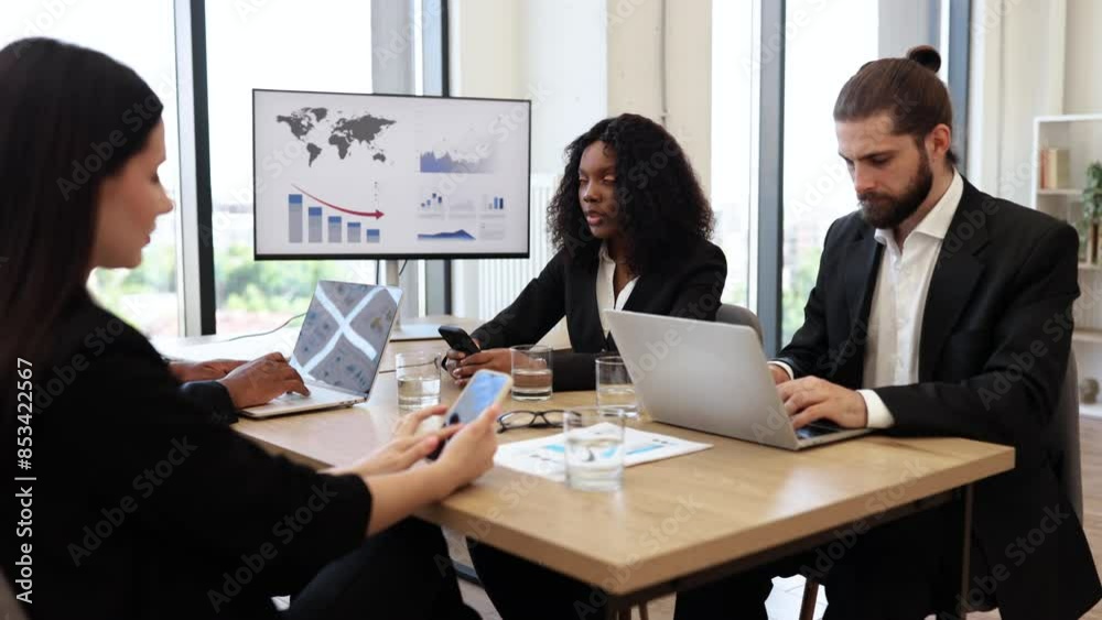 Diverse business team engaged in serious discussion using electronic devices during meeting room presentation, digital charts on screen. Diverse business team engaged in serious discussion using electronic devices during meeting room presentation, digital charts on screen.