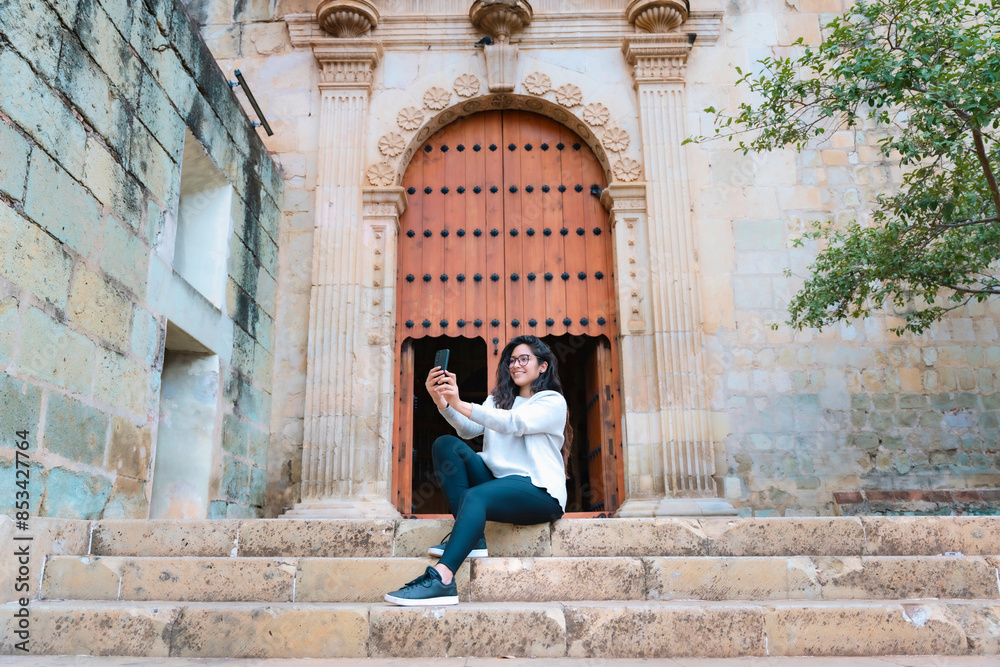 Latin woman taking selfie on church steps. Urban photography in Oaxaca, Mexico. Taken at Santo Domingo church. People and heritage concept. Latin woman taking selfie on church steps. Urban photography in Oaxaca, Mexico. Taken at Santo Domingo church. People and heritage concept.