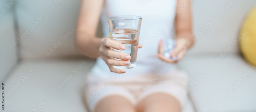 woman hand holding medicine painkiller pill and water glass on the sofa at home, taking for headaches, stomach ache, Diarrhea Pain from food poisoning, Endometriosis, Hysterectomy and Menstrual woman hand holding medicine painkiller pill and water glass on the sofa at home, taking for headaches, stomach ache, Diarrhea Pain from food poisoning, Endometriosis, Hysterectomy and Menstrual