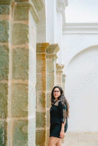 Young Latina woman enjoying a sunny day while walking through historical sites in Oaxaca, Mexico, wearing a black dress and sunglasses.