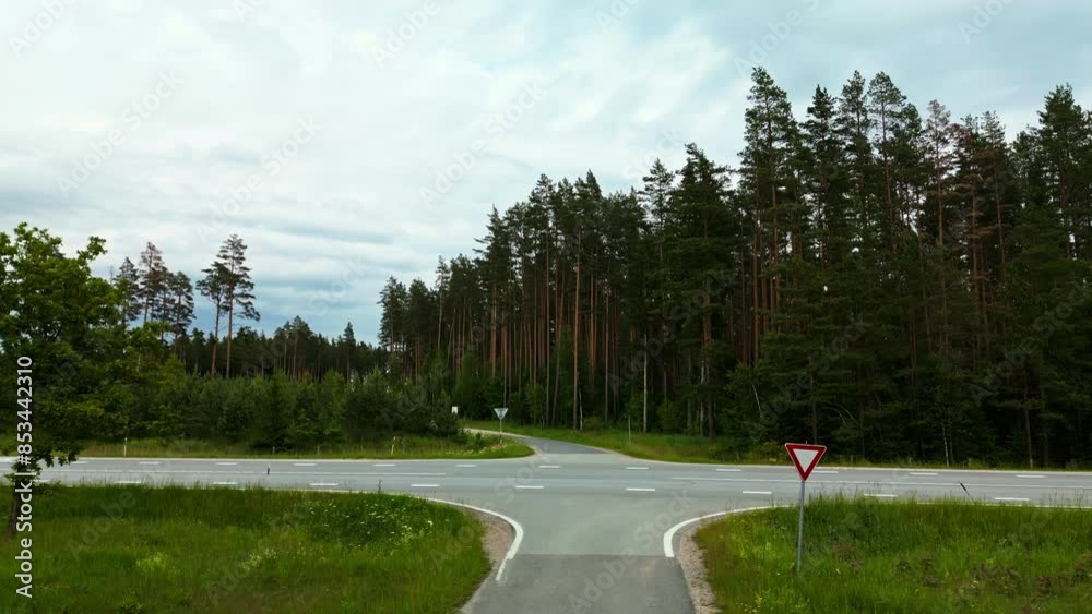 Aerial view of a red car crossing rural intersection, surrounded by lush forest, depicting beautiful natural landscape Aerial view of a red car crossing rural intersection, surrounded by lush forest, depicting beautiful natural landscape
