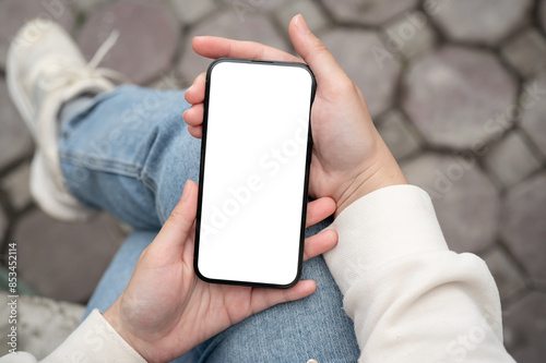 Foto A woman holding a smartphone with a white-screen mockup over her lap while sitting outdoors