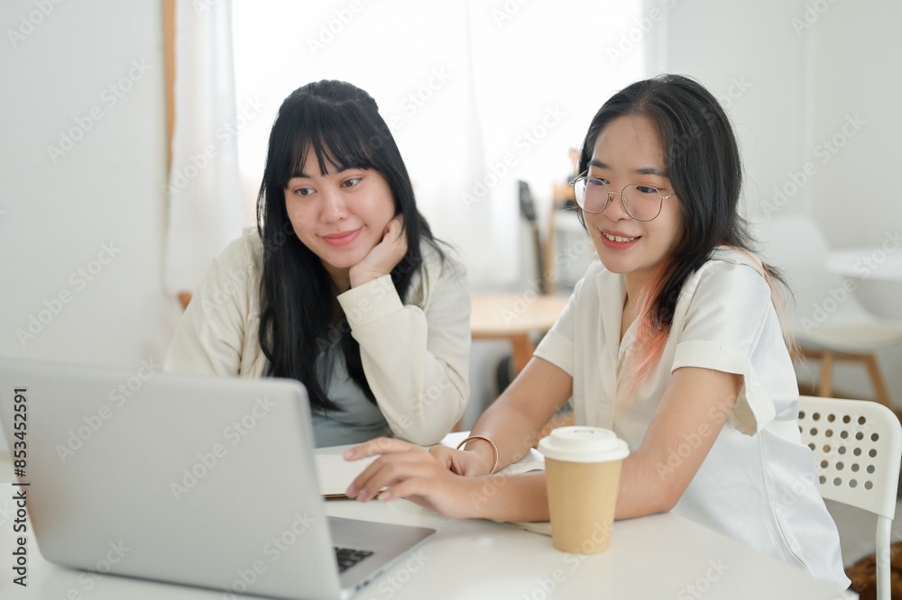 Two students are meeting at a cafe to work on a co-project or study together, looking at a laptop. Two students are meeting at a cafe to work on a co-project or study together, looking at a laptop.