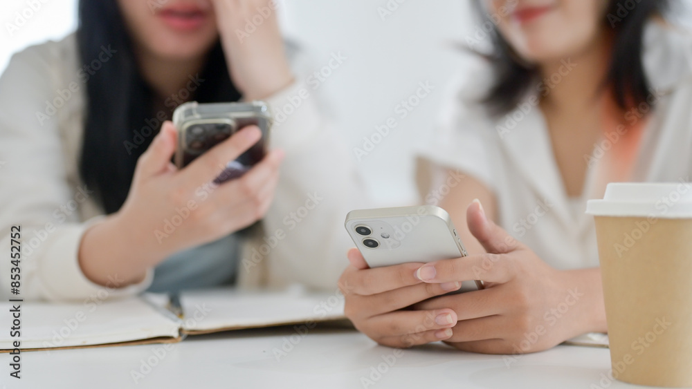 Two young Asian female friends are scrolling on their smartphone while sitting in a cafe together. Two young Asian female friends are scrolling on their smartphone while sitting in a cafe together.