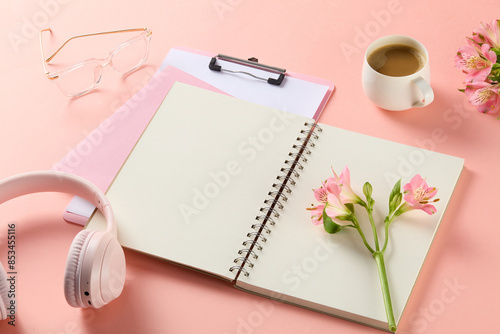 Top view at pink office working tabletop, in the middle displays an empty note book, which has a branch of narcissus above. Product presentation and advertising space