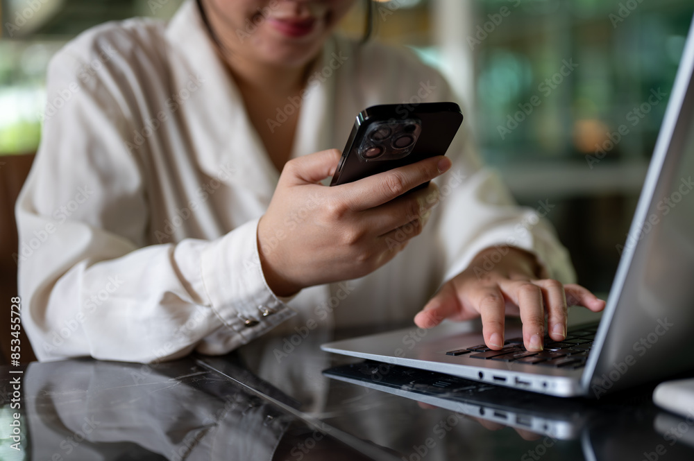A cropped image of a businesswoman is multitasking, using her smartphone and laptop computer. A cropped image of a businesswoman is multitasking, using her smartphone and laptop computer.
