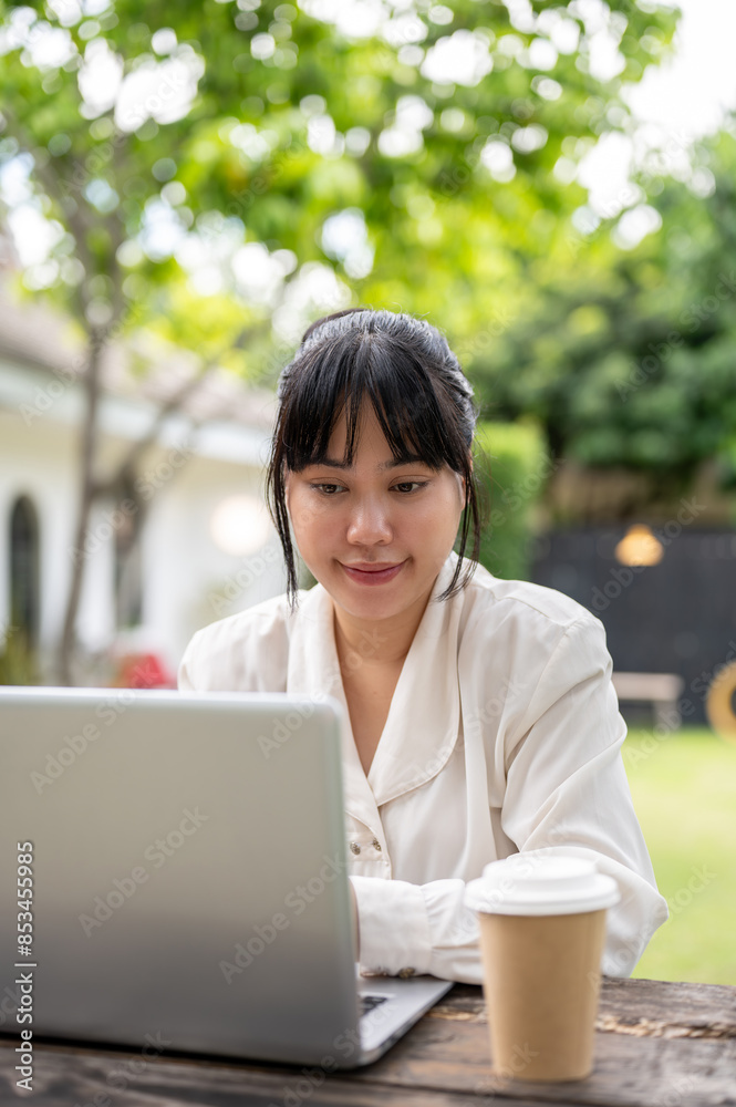 A businesswoman working remotely from a backyard, working on her laptop computer at a wooden table. A businesswoman working remotely from a backyard, working on her laptop computer at a wooden table.