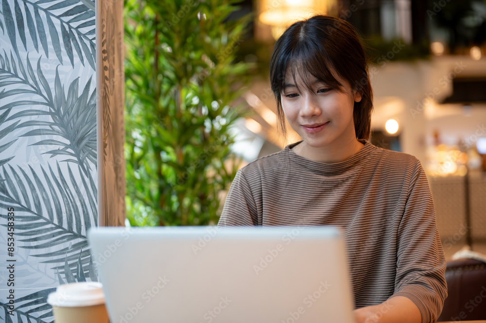 A young attractive Asian woman working remotely from a coffee shop, working on her laptop computer. A young attractive Asian woman working remotely from a coffee shop, working on her laptop computer.