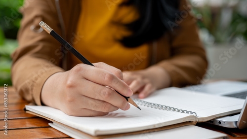 Vászonkép A close-up image of an Asian woman holding a pencil, writing something in her notebook