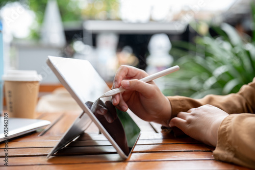 A side view image of a woman drawing or writing something on her digital tablet with a stylus pen. photo